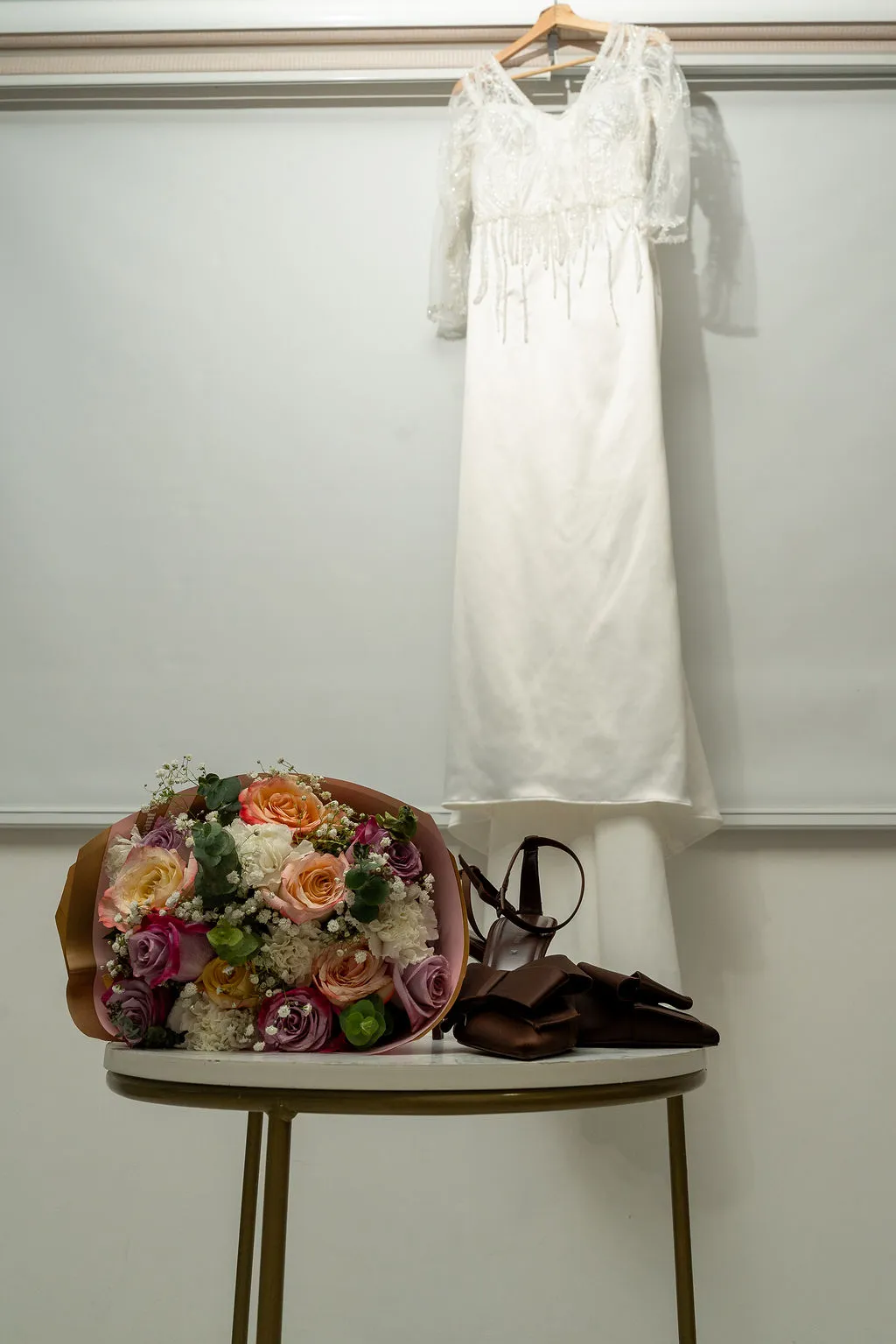 Vestido de novia colgado junto al ramo y los zapatos antes de la boda